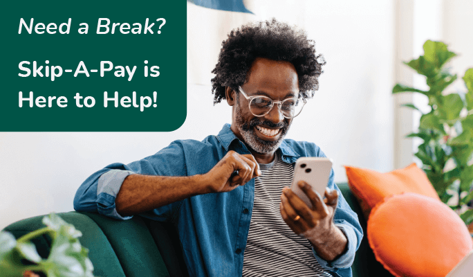 Need a break? Skip-A-Pay is here to help! Man smiling while using his cell phone.