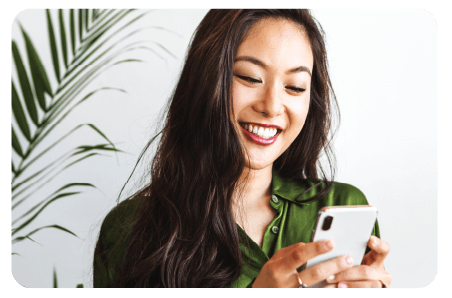 Asian woman holding a cell phone by plants and smiling