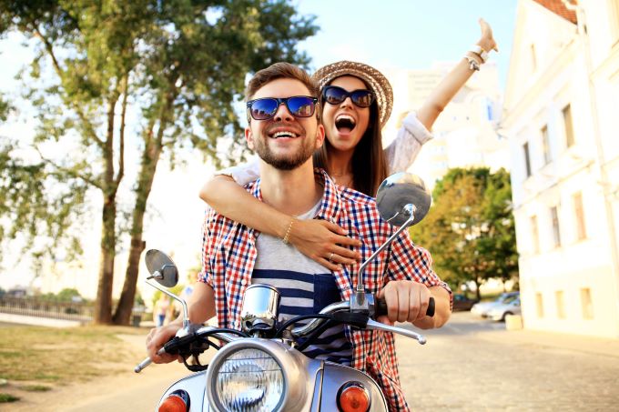 happy couple riding scooter through town